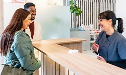 Dental receptionist smiling at couple in lobby