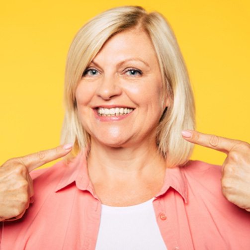 Mature woman pointing at her smile with All on 4 dental implants in Idaho Falls