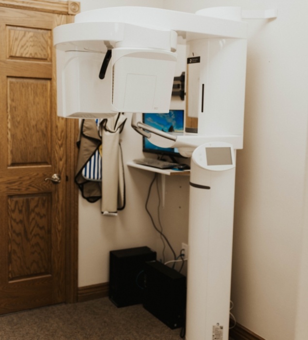 Dental cone beam C T scanner next to screen showing scans of mouth and jaw