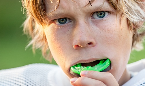 Teen boy placing green athletic mouthguard into his mouth
