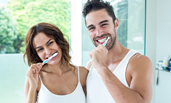 Smiling man and woman brushing their teeth