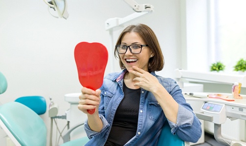 Woman looking at her smile in mirror in dental chair