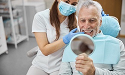 Man in dental chair looking in mirror and smiling