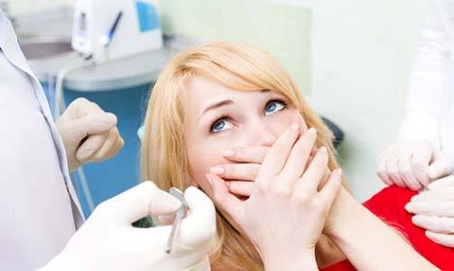 Woman in dental chair covering her mouth in fear