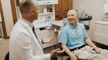 Older man in blue polo shirt talking to dentist