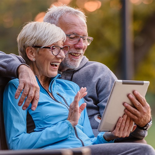 Smiling older couple holding tablet while having virtual smile consultation in Idaho Falls