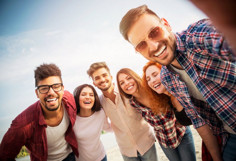 Patient smiling with friends on the beach after cosmetic dentistry