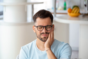 Man with glasses and beard rubbing jaw in pain